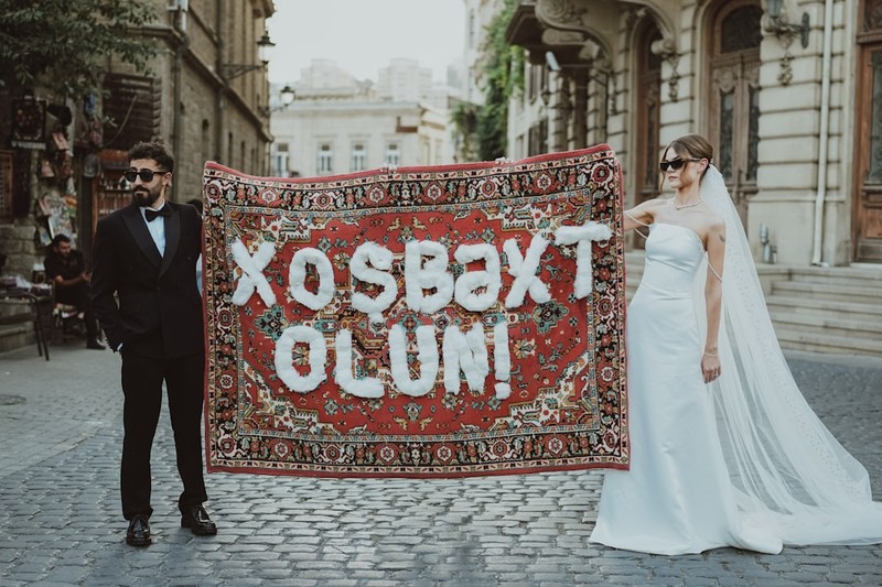 A bride and groom hold a carpet with balloon letters.
