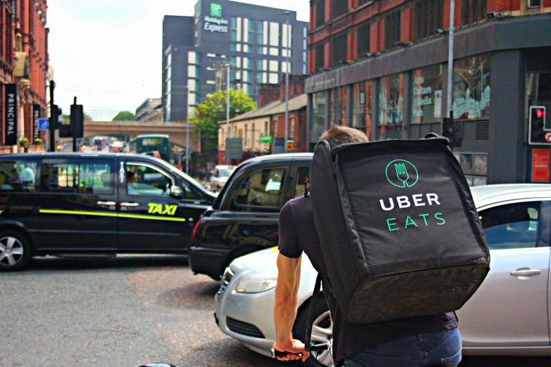 An Uber Eats delivery cyclist rides along a busy urban street with branded backpack visible