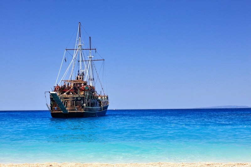 A classic pirate-style sailing ship anchored in turquoise waters near a sandy beach