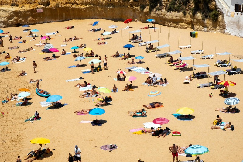 A crowded beach in Faro, Portugal filled with sunbathers and colorful umbrellas on a hot day