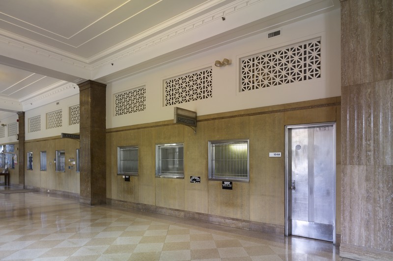 Interior lobby of a federal courthouse with columns, service windows, and checkered tile floor