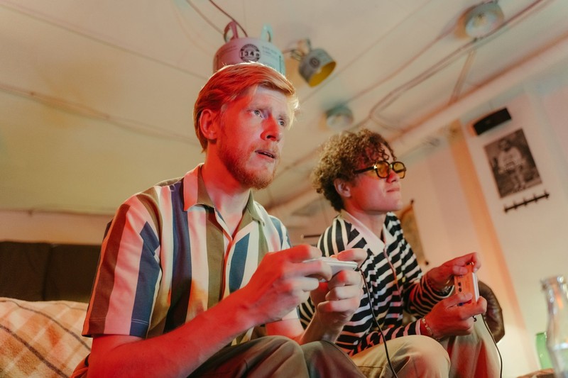 Two people playing video games with controllers on a couch in a cozy, warmly-lit room