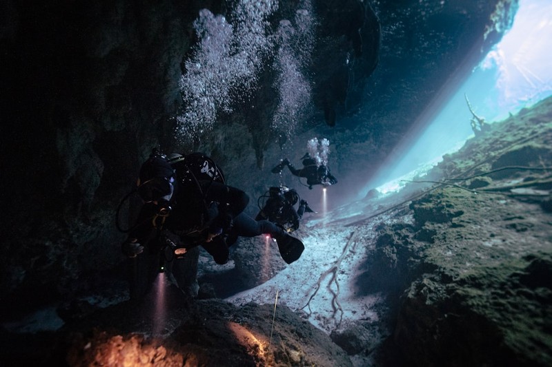 Scuba divers exploring an underwater cave with dramatic lighting