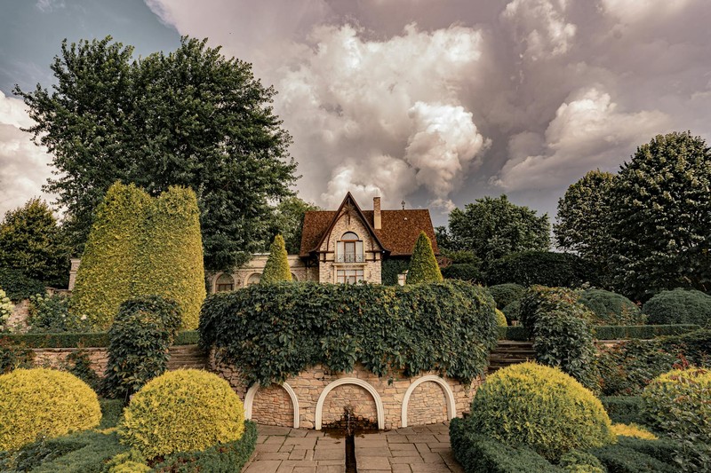 An elegant manor house surrounded by formal topiary gardens under a dramatic cloudy sky