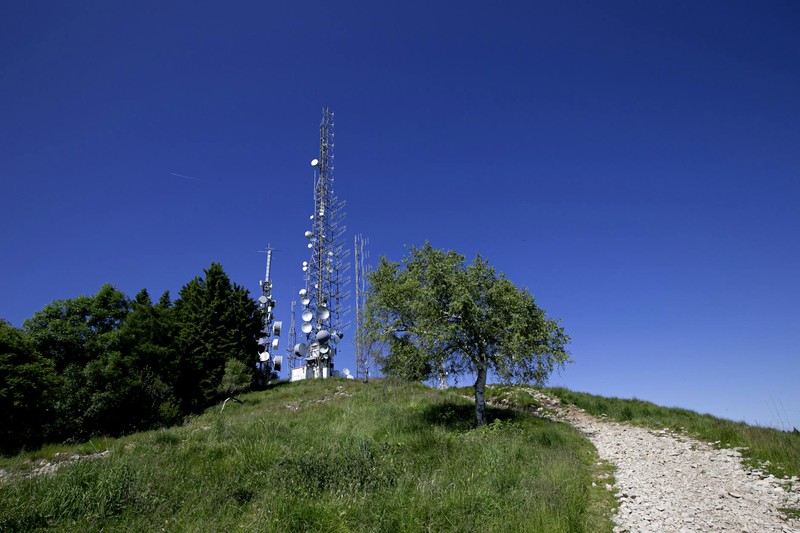 Broadcast communication towers atop a grassy hill under a blue sky