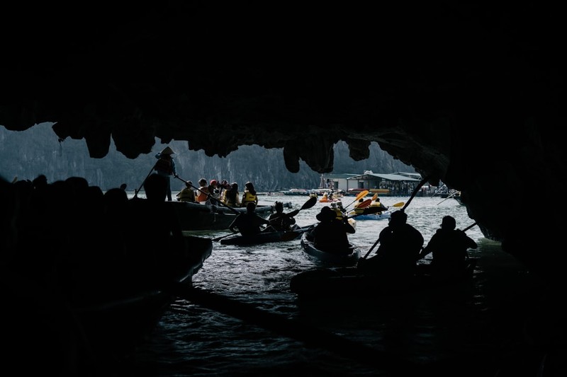 Silhouetted figures in boats emerge from a dark cave opening into daylight