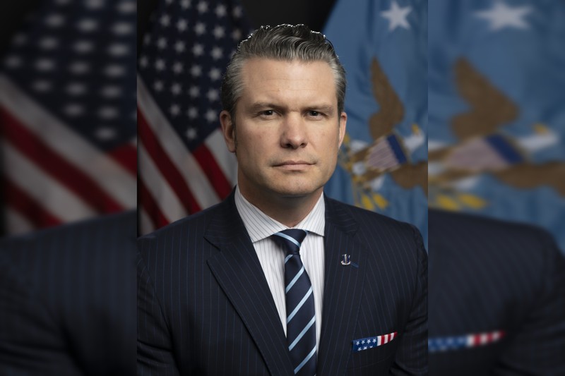 Official portrait of Secretary of Defense Pete Hegseth with American and military flags in the background