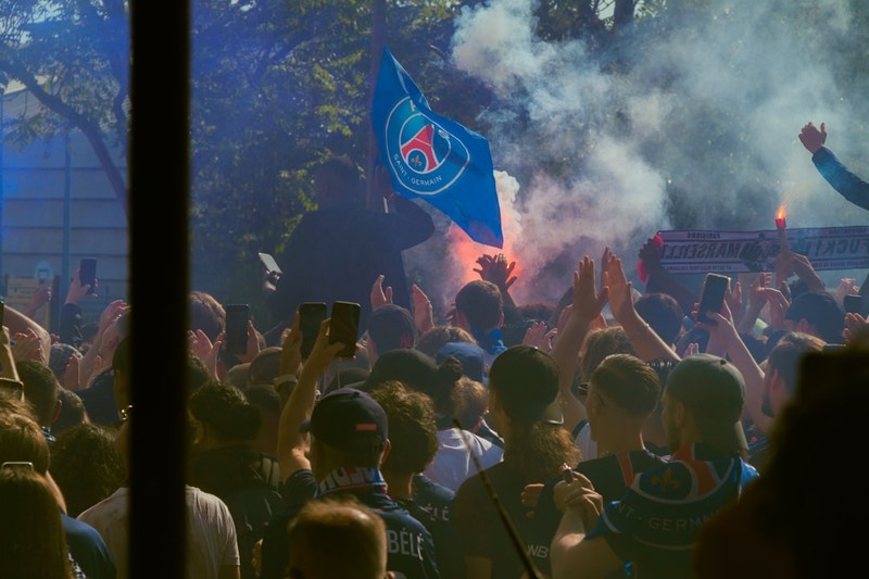 PSG fans celebrate with flares and a club flag in a crowded outdoor gathering