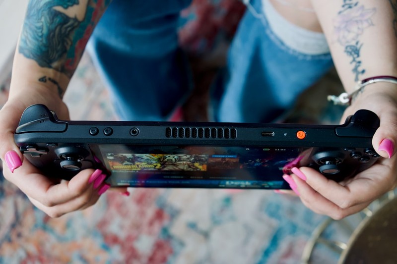 A person's hands holding a Steam Deck handheld gaming console, actively playing a colorful game