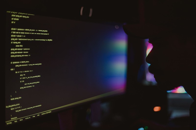 Silhouette of a solo programmer coding at a desk illuminated by monitor glow in a dark room