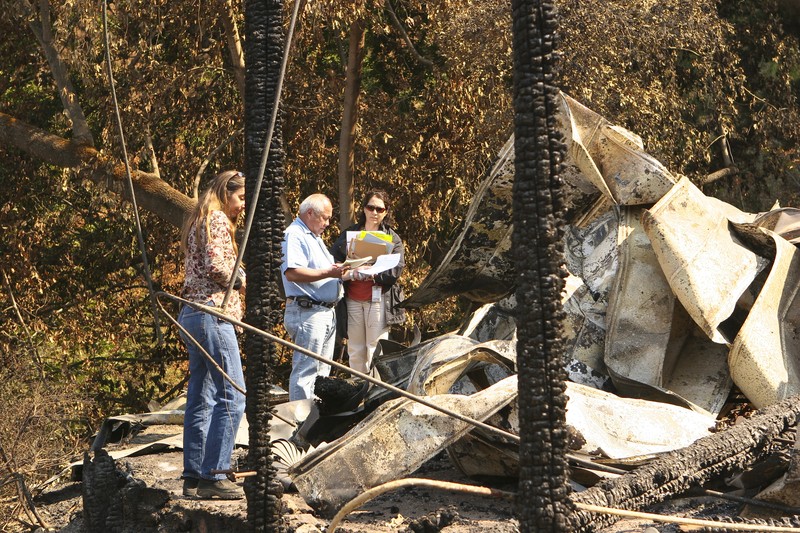 Damage assessment team inspecting the charred remains of a home destroyed by wildfire in a wooded area