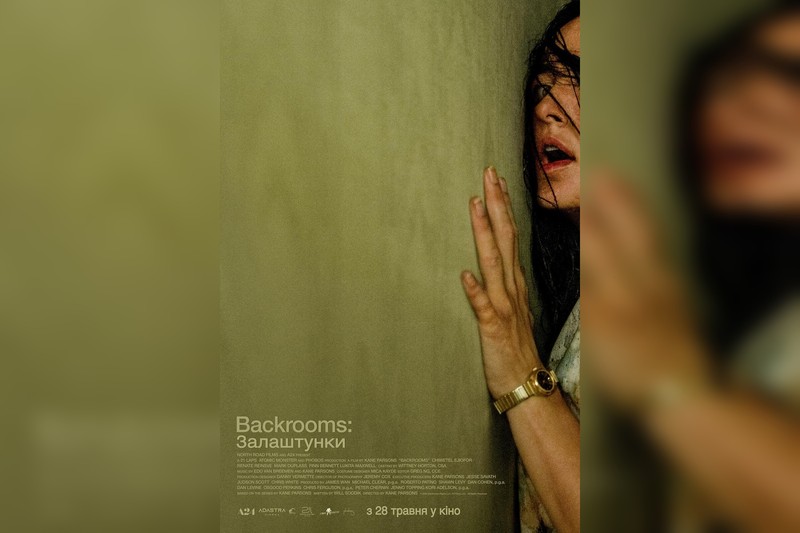A person presses their hand against a dimly lit textured wall in a tense scene from The Backrooms