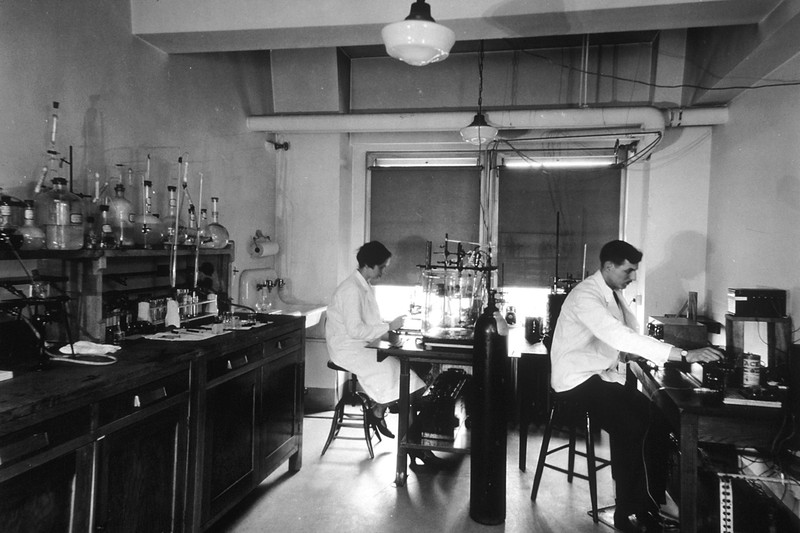 Two scientists in white lab coats working at benches in a cancer research laboratory