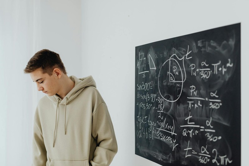 A young person in a hoodie stands beside a blackboard covered with mathematical equations and geometric diagrams