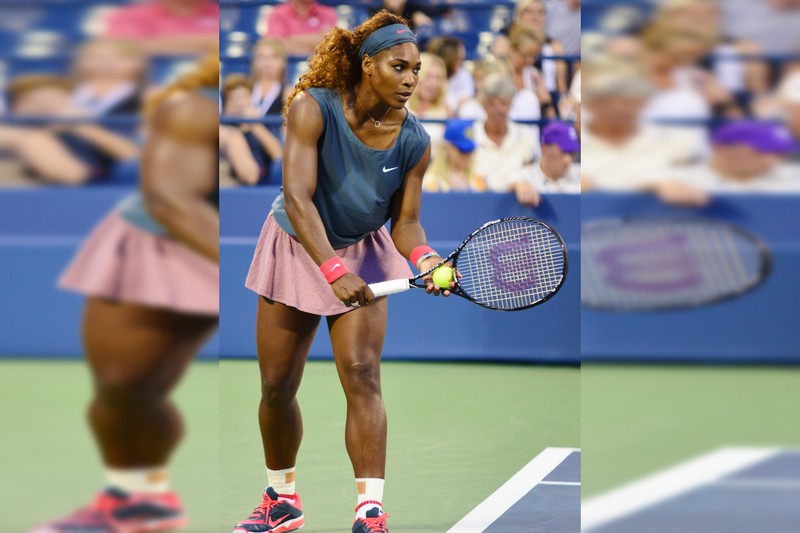 Serena Williams in a ready stance during a doubles match at the 2013 US Open, wearing a teal Nike top and pink skirt with racket in hand
